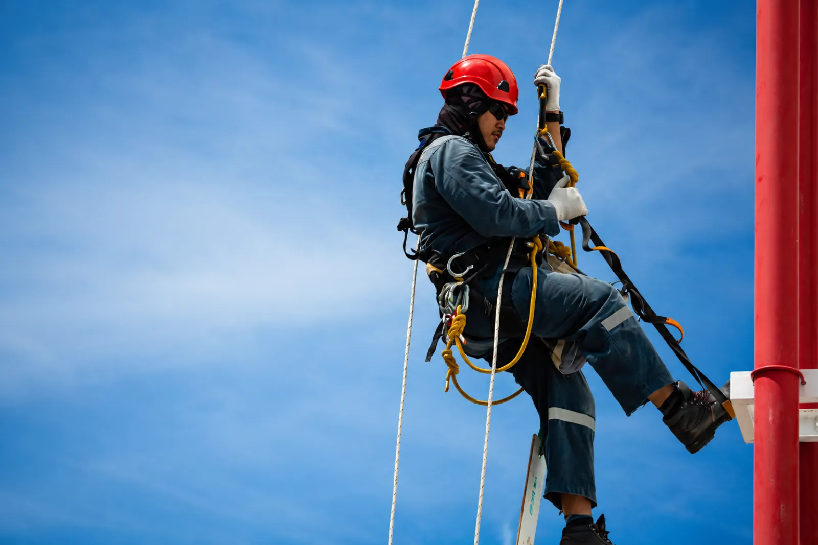 Técnico de acesso por corda com capacete vermelho e talabarte em operação